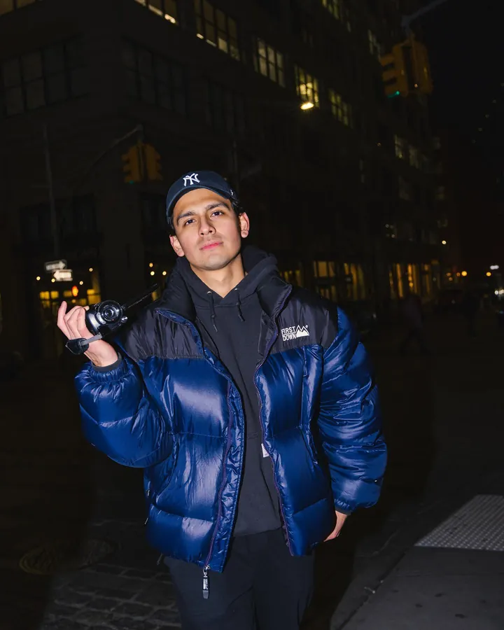 Man in a blue puffer jacket holding a camera on a street at night
