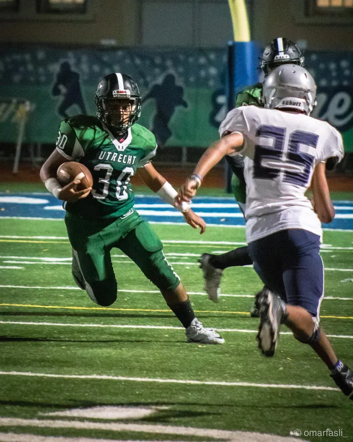 Football player in green running the ball past a defender