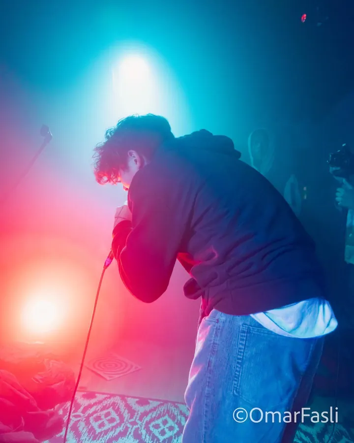 Performer leaning into a microphone under a red and blue flare