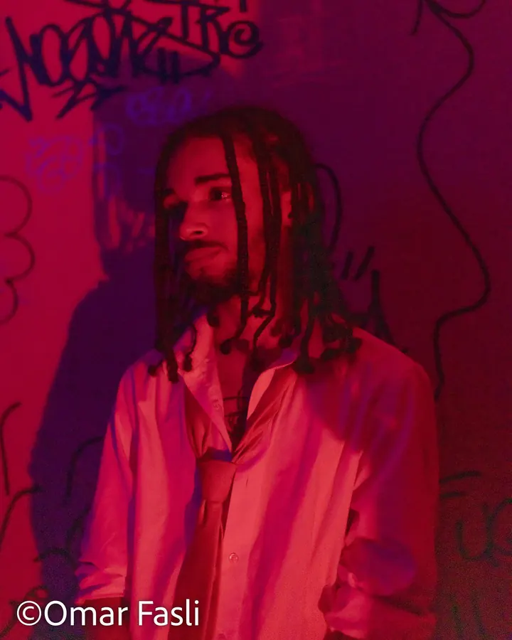 Man with long hair against a red graffiti wall