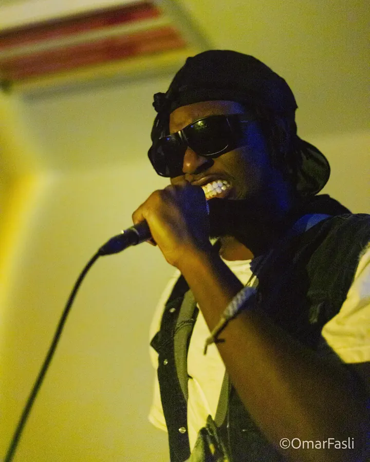 Performer in sunglasses singing into a microphone in yellow light
