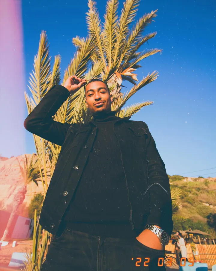 Man in black posing under palm trees, low angle