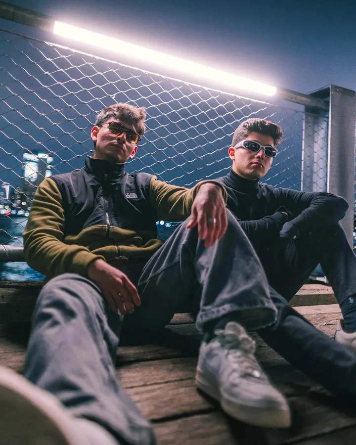 Two men sitting against a fence on a pier at night