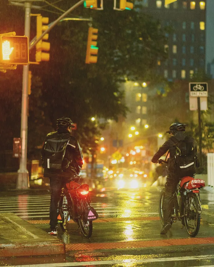 Delivery riders at a rainy intersection at night