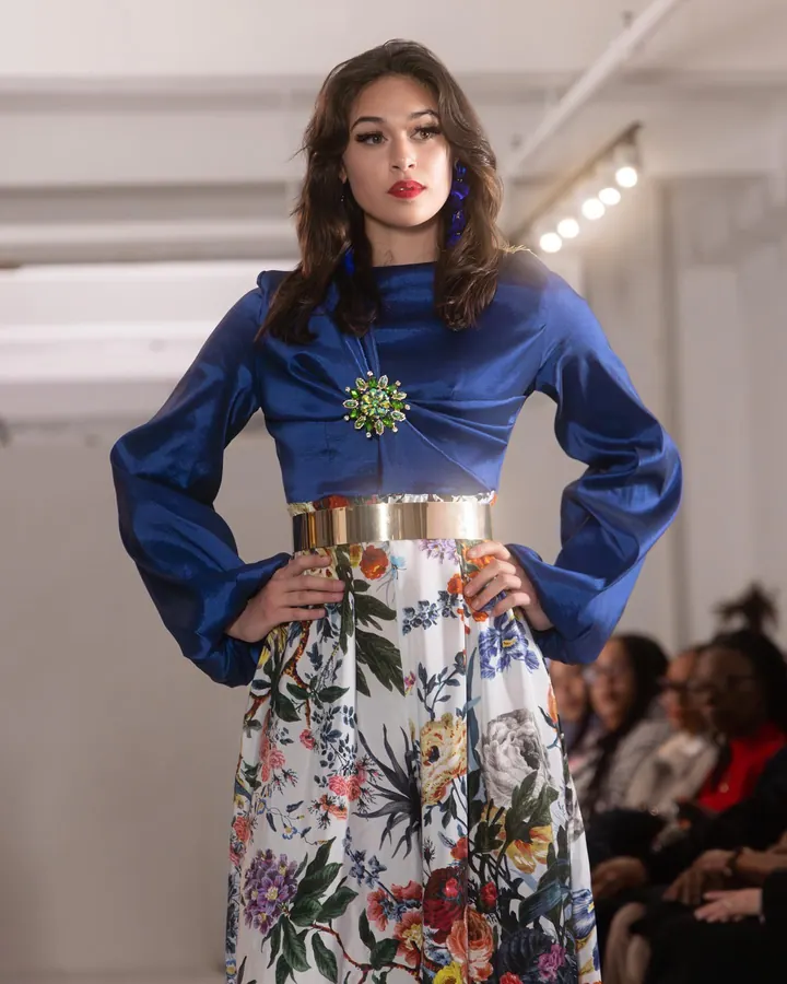 Model in a blue blouse and floral skirt on the runway