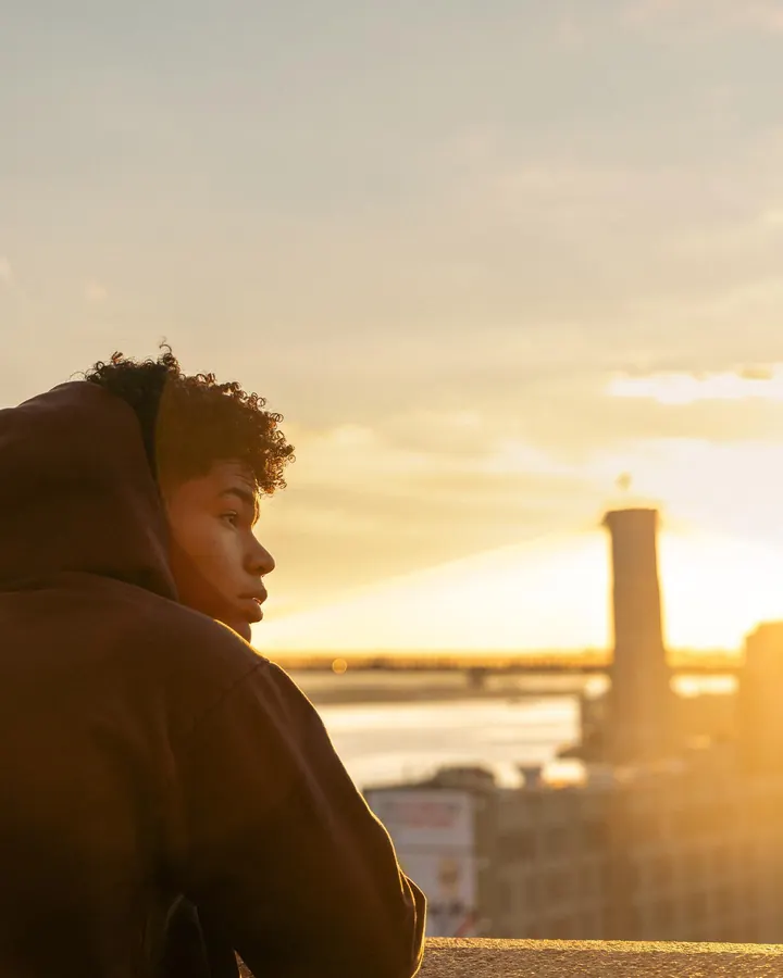Man in a hoodie in profile against a sunrise over the bridge